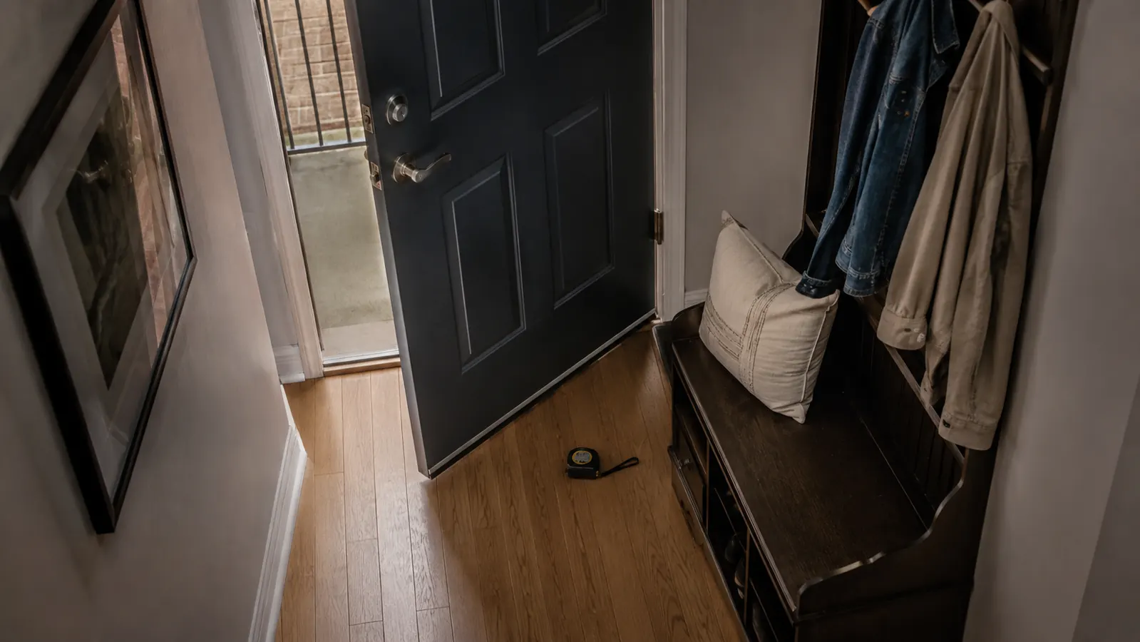 A narrow apartment hallway with a front door swinging open just inches from the edge of a hall tree bench, showing how tight the clearance really is