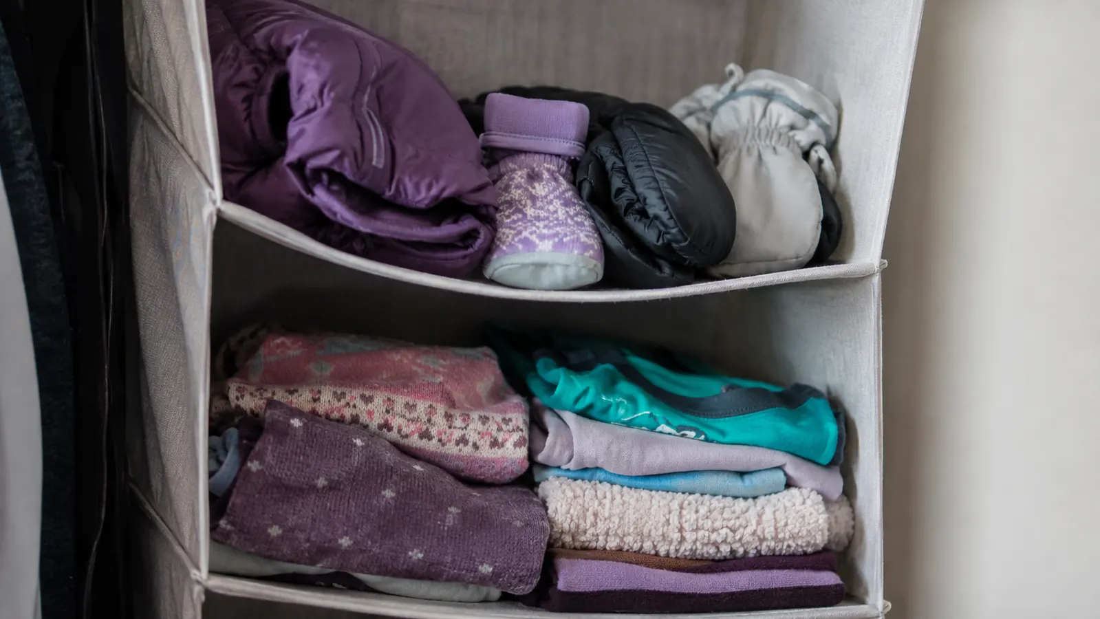 Two kids' snow gear and gear bins neatly stacked on the top shelves of a hanging closet organizer