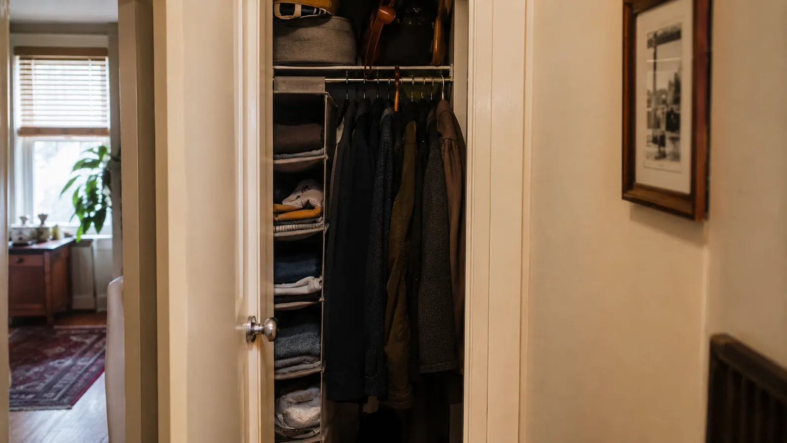 Narrow apartment hallway closet with coats and a gray hanging shelf organizer, soft morning light