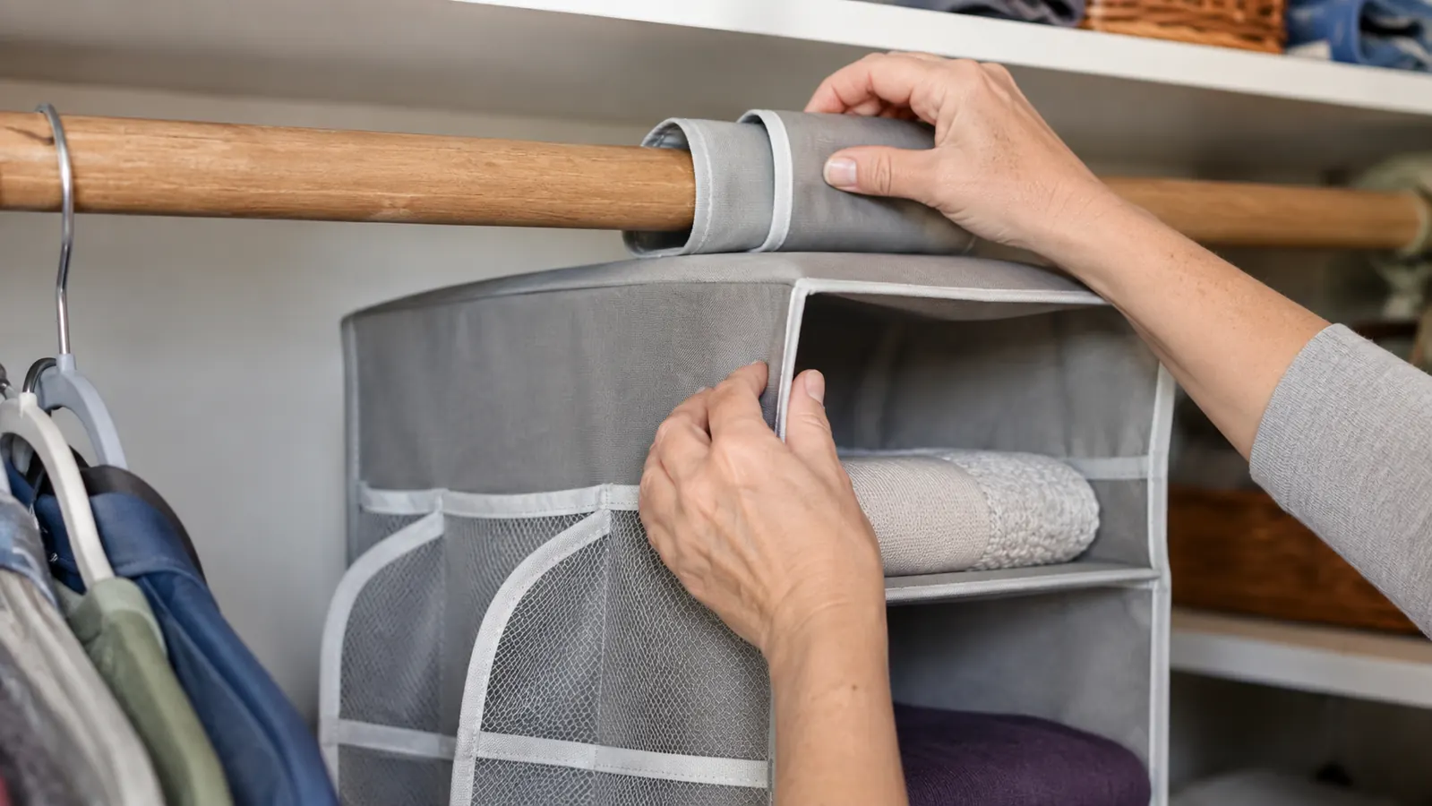 Hands clipping a gray hanging closet organizer onto a wooden closet rod